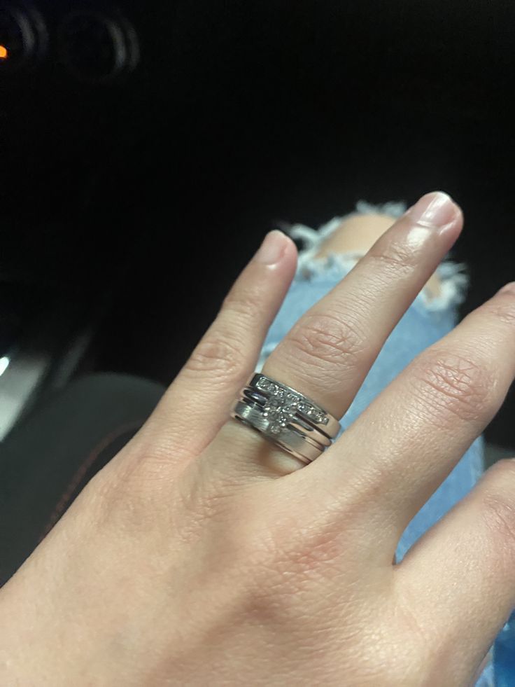 a woman's hand with two wedding bands on her fingers, in front of a car