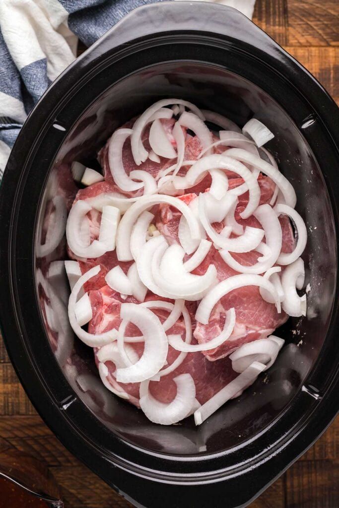 an overhead view of onions and meat in the slow cooker on a wooden table