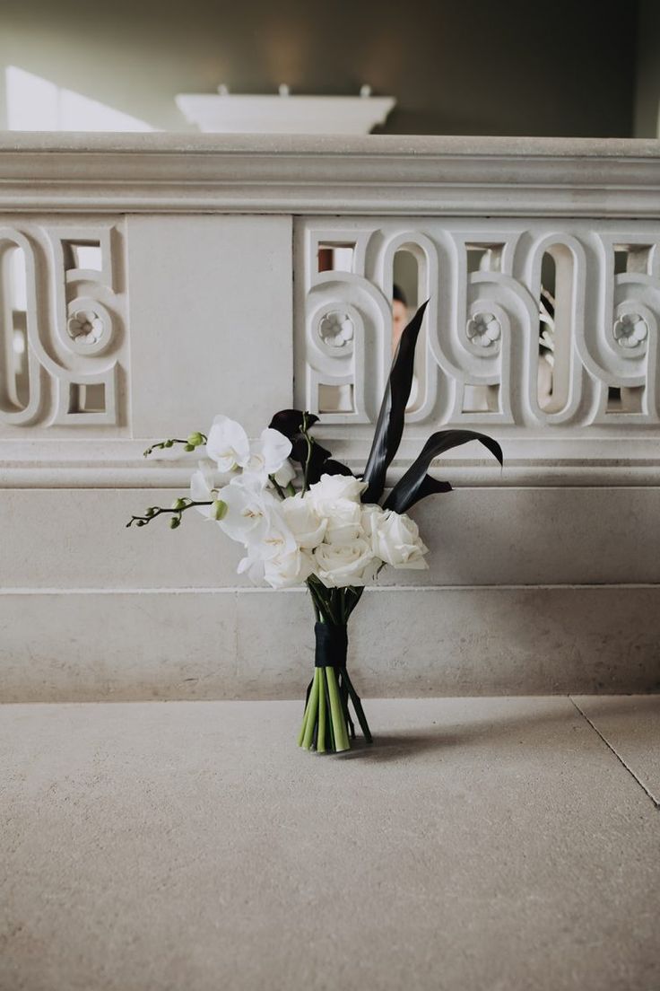 a vase filled with white flowers sitting on top of a stone floor next to a wall