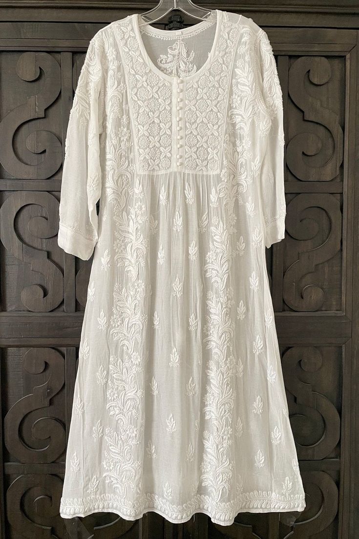 This White Muslin Silk Handcrafted Lucknowi Chikankari A Line Kurta Long Dress is a stunning piece of art. The beautiful white  dress  is perfect for any special occasion. The luxurious fabric and intricate Lucknowi Chikankari embroidery make it a timeless piece that will never go out of style.    Muslin silk    Length 48" inches   Long sleeves 18" inches  Round neck  A line   Lucknowi chikankari hand embroidered    Dry Clean    Fit:     True to size    Inside Margin:     No    Disclaimer:   Sin Transitional White Dress With Intricate Embroidery, Traditional White Maxi Dress, Transitional White Cotton Dress, Long White Festive Dress, Festive Long White Dress, Fitted Chikankari Embroidery Dress For Transitional Season, White Anarkali Dress For Eid, Bohemian Dresses With Chikankari Embroidery For Transitional Season, White Fitted Anarkali Dress