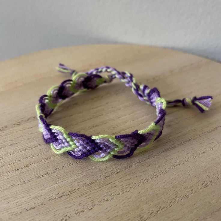 a purple and green braided bracelet sitting on top of a wooden table next to a white wall