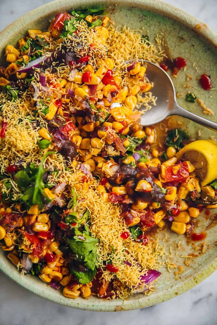 a bowl filled with corn and vegetables on top of a marble table next to a spoon