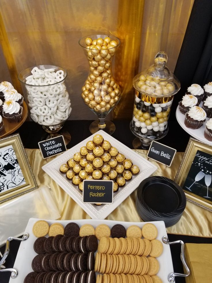 an assortment of desserts and candies displayed on a table with black and gold accents