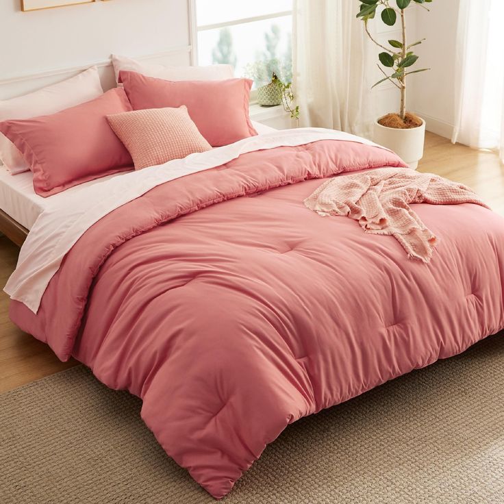 a bed with pink comforters and pillows in a room next to a potted plant