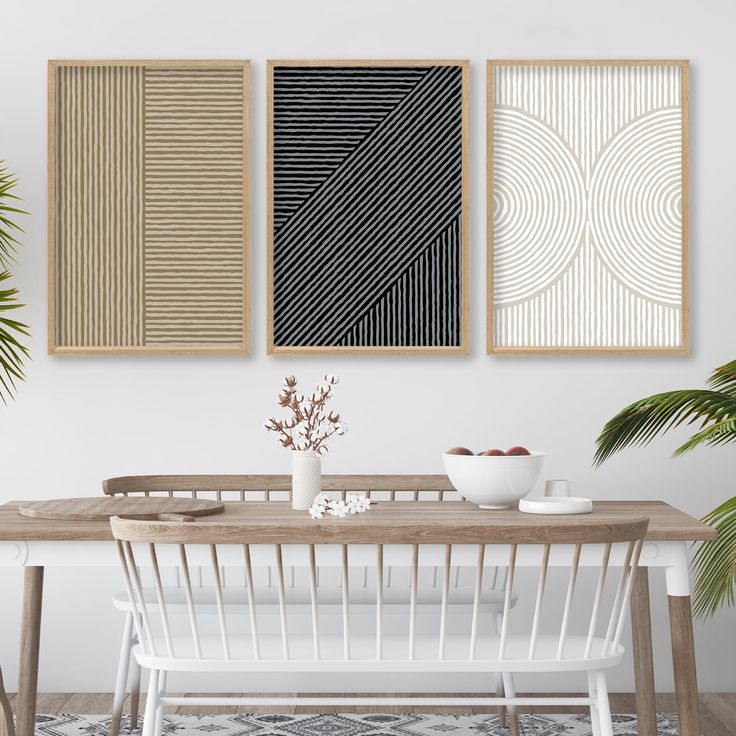 three abstract paintings hang on the wall above a dining room table with white chairs and a plant