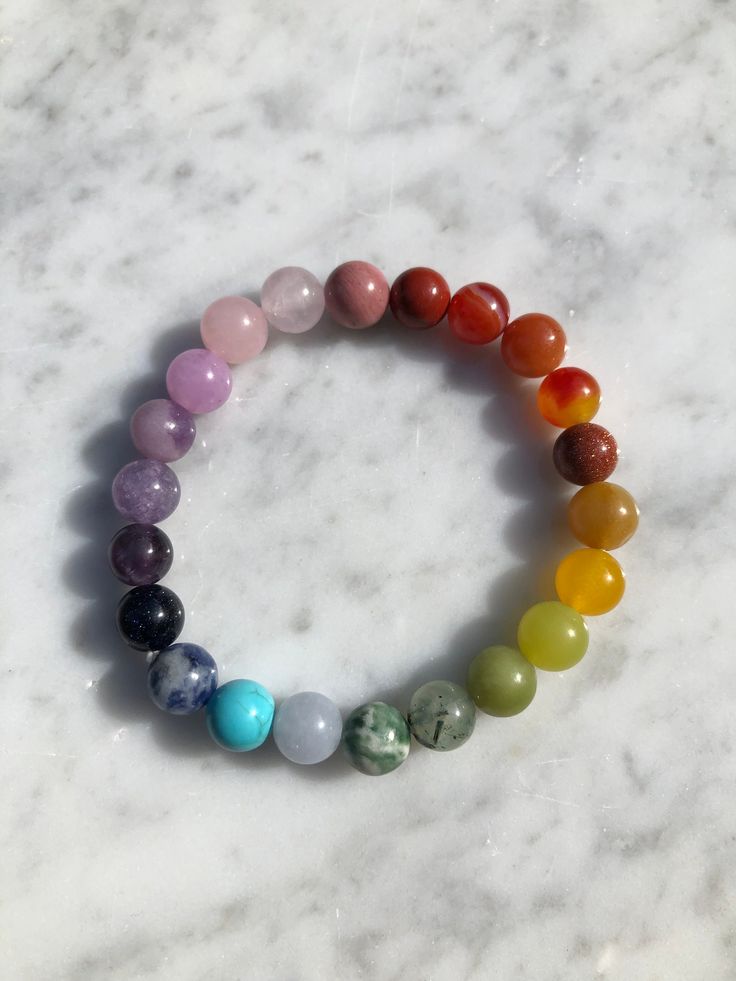 Introducing our exquisite handmade Chakra Gemstone bracelet. This stunning design features a combination of Red Jasper, Orange Carnelian, Red and Yellow Aventurine, Lemon Jade, Peridot, Green Moss Agate, Green and Blue Spot Jasper, Purple Dyed Chalcedony, Kunzite, Blue Magnesite, Goldstone, and Rhodonite. Each stone in this design is a a celebration of the vibrant colors found in nature and each holds its own unique hue, representing different aspects of the natural world. Beads are 8mm each, on a stretch cord which is double strung for durability. Each bracelet is carefully placed on a selenite plate overnight to cleanse and recharge its energy, ensuring it has the highest vibrational quality.  From the grounding red of Red Jasper to the soothing blue of Blue Magnesite, these colors reson Multicolor Crystal Bracelet With Round Natural Stones, Multicolor Agate Crystal Bracelet With Round Beads, Rainbow Gemstone Beads Bracelet, Rainbow Gemstone Beads Bracelets For Healing, Rainbow Gemstone Beads Bracelet For Healing, Rainbow Gemstone Beads Healing Bracelet, Rainbow Natural Stones Beaded Bracelets For Jewelry Making, Multicolor Crystal Gemstone Bracelet For Healing, Multicolor Natural Stone Beaded Bracelets