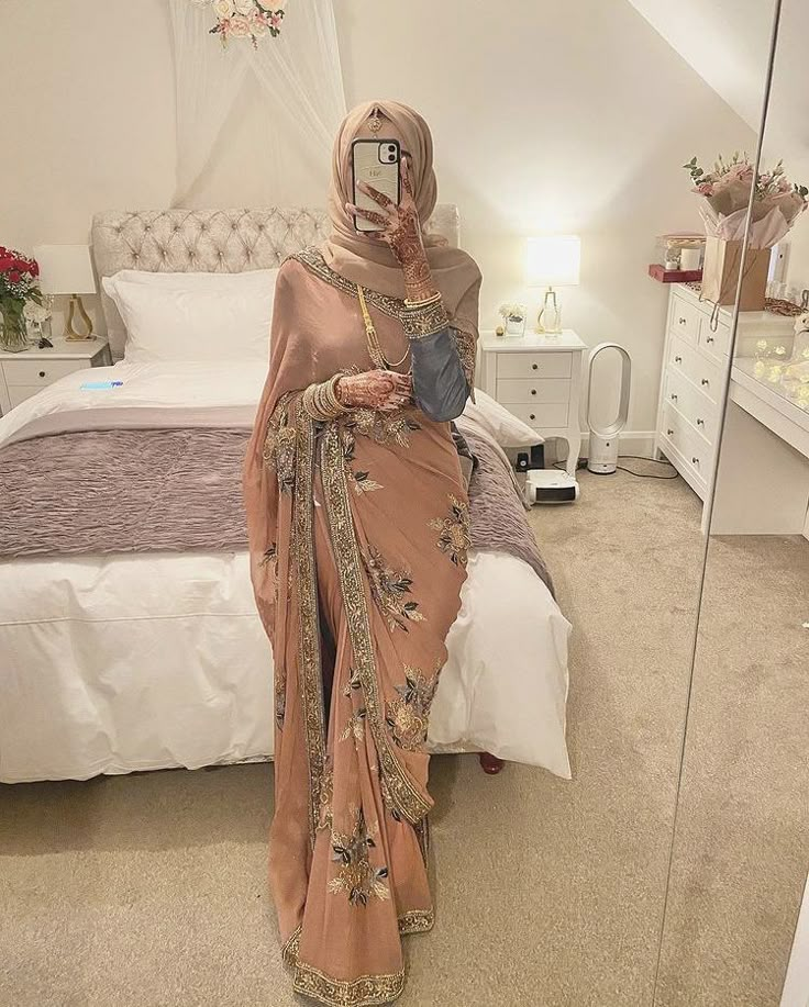 a woman in a hijab taking a selfie with her cell phone on the bed