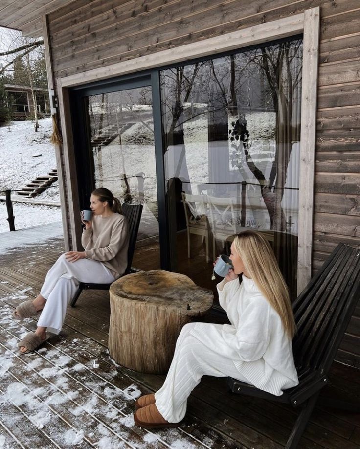 two women are sitting outside in the snow drinking coffee and talking on their cell phones