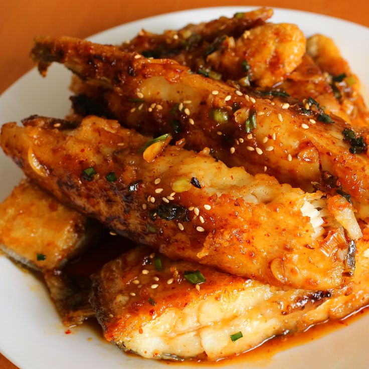 a white plate topped with chicken wings covered in sesame seeds and seasoning on top of a wooden table