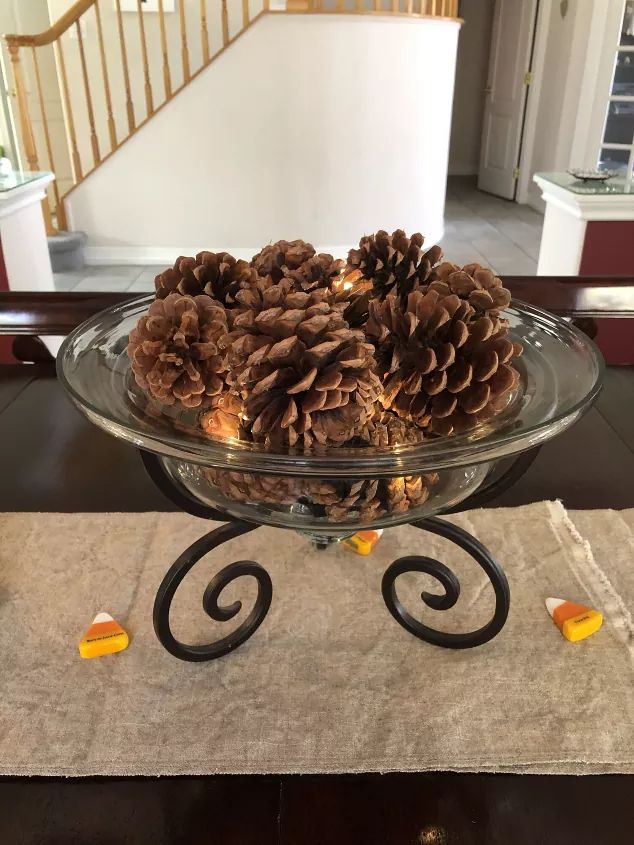 a glass bowl filled with pine cones sitting on top of a table next to a stair case