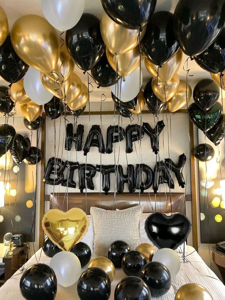 black and gold balloons are hanging from the ceiling in front of a happy birthday sign