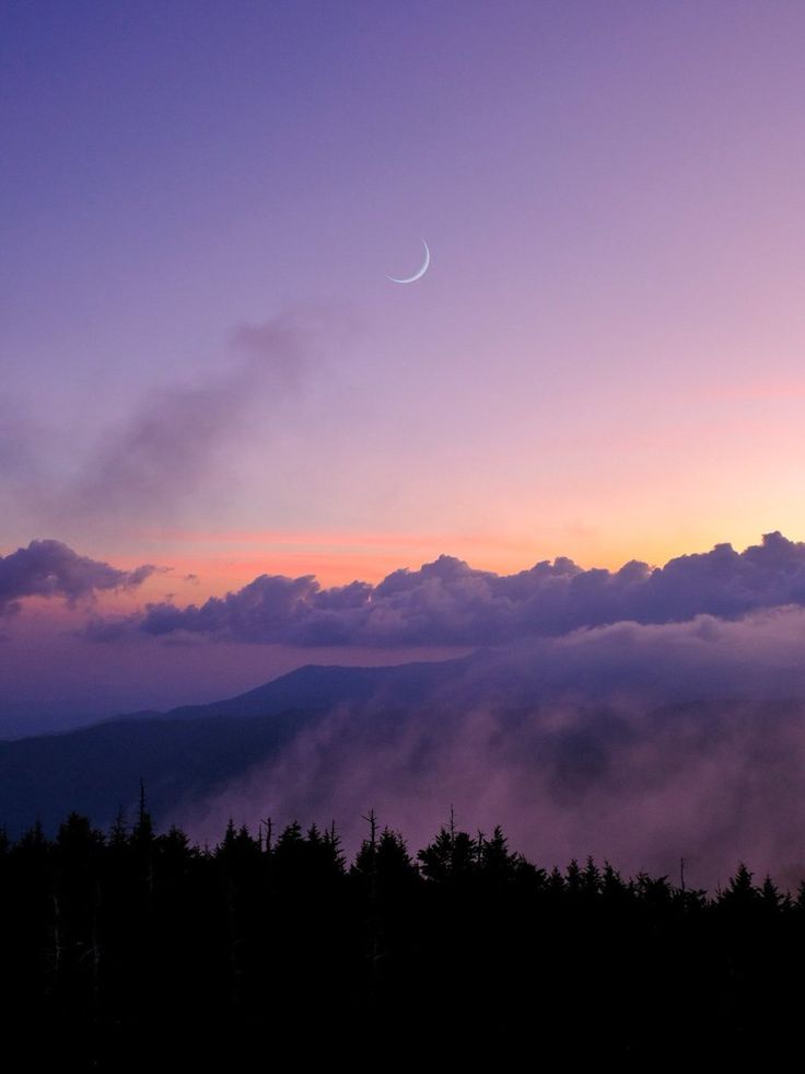 the sun is setting over some trees and mountains in the distance, with a crescent above them