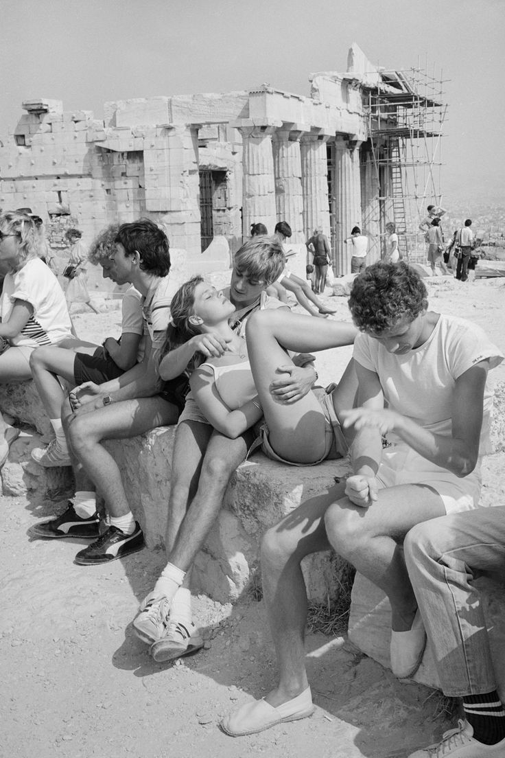 a group of people sitting on top of a stone wall next to the ruins of an ancient building