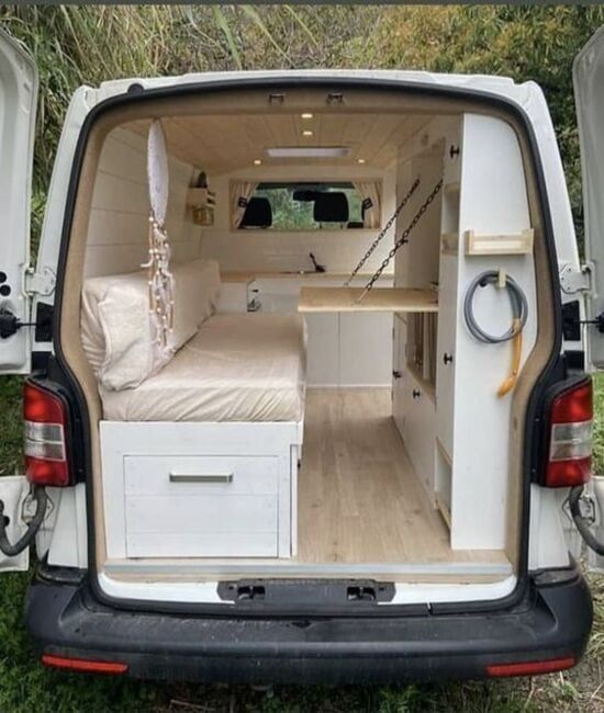 the back end of a van that is parked on grass with its door open and bed in it