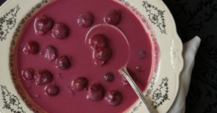 a bowl of soup with cherries in it and a spoon next to it on a plate