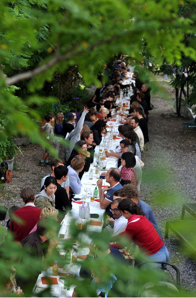 a group of people sitting around a long table in the middle of an outdoor area