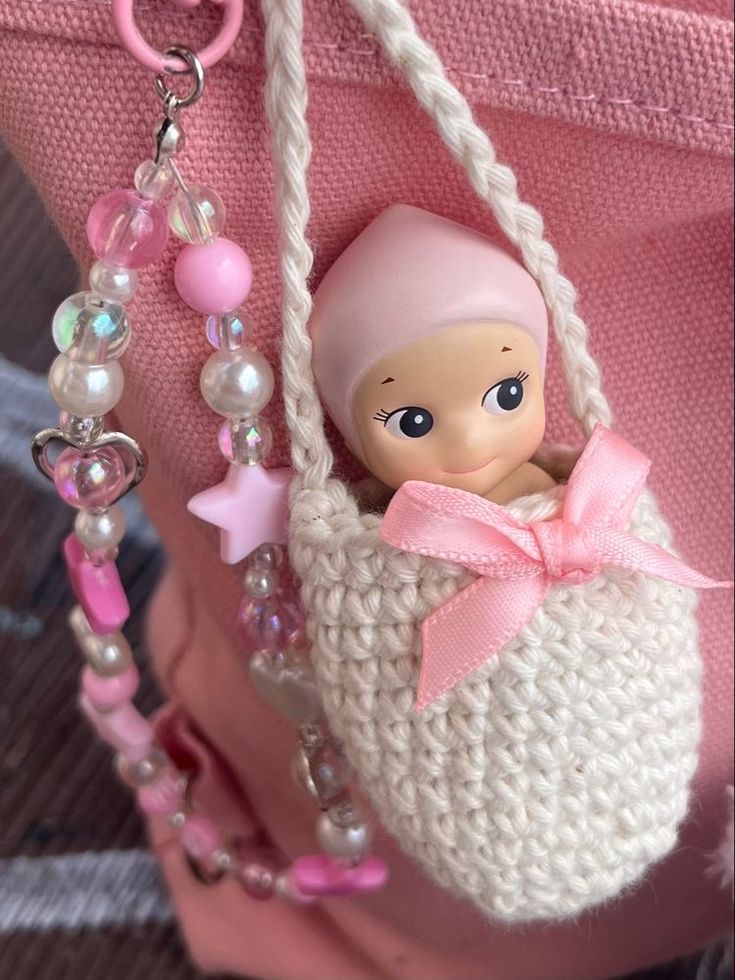 a small doll in a purse with pearls and beads on it's chain hanging from a pink handbag