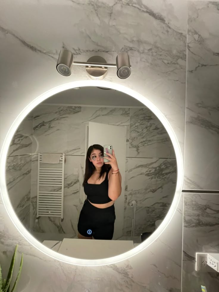 a woman taking a selfie in front of a bathroom mirror with the lights on