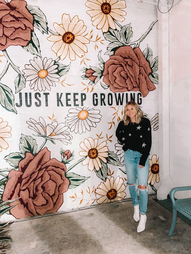 a woman standing in front of a wall with flowers on it and the words just keep growing