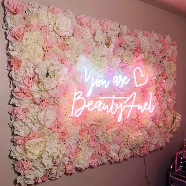 a flower wall with the words you are beautiful written in neon letters on it and surrounded by flowers