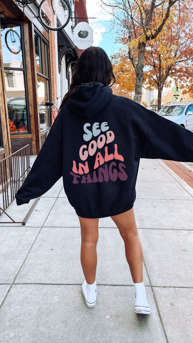 "This oversized hoodie is the perfect way to stay cozy and comfy while looking stylish. The unisex design features a hood, long sleeves, and a kangaroo pocket. The back proudly displays the words \"See Good In All Things\" in a bold retro wavy font to remind the person behind you of the good in life. The hoodie is made from super soft fabric for extra comfort, and the relaxed fit ensures you'll look great no matter how you wear it. Gildan 18500 50% cotton, 50% polyester Medium-heavy fabric  Classic fit Tear-away label Runs true to size Let me know if you have any questions! Xo, Bobbi" Positive Message Hoodie, Printed Hoodies Ideas, Hoodie Design Ideas Aesthetic, Trendy Hoodie Designs, Quotes Hoodies, Oversized Hoodie Outfit, Hoodie Design Ideas, Wavy Font, Motivational Hoodies