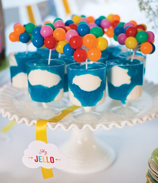 blue jello cups filled with candy and balloons on top of a white cake plate