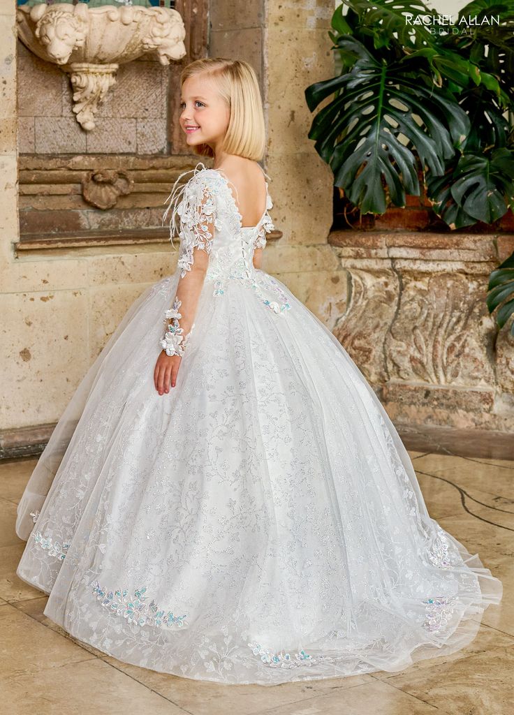 Your sweet girl will love twirling around in this lace applique long full length sleeve feather dress with A-line skirt by Rachel Allan RB9149. This Rachel Allan flower girl dress is enchanting with its delicate glitter tulle adorned with subtle AB accents. The gown features a charming V-neckline and sheer sleeves, both embellished with intricate lace detailing that adds a touch of elegance. The voluminous tulle skirt is gracefully layered, making it perfect for a little girl to twirl in joy on a special day, ensuring she feels like a princess alongside the bride. Girls Feather Long Sleeve Gown by Rachel Allan RB9149 Rachel Allan Flower Girl/First Communion Collection: Fall 2024 Style Number: RB9149 Fabric: Beading, Applique, Tulle, Glitter Tulle, Feathers, 3D Flowers Please note: There ma Long Sleeve Tulle Dress For Confirmation, Princess Dress With Long Sleeves And Tulle Skirt, Princess Style Long Sleeve Dress With Tulle Skirt, Long Sleeve Lace Dress With Fitted Bodice, Long Sleeve Lace Ball Gown With Lace Bodice, Princess Style Long Sleeve Dress For Debutante Ball, Fitted Long Sleeve Gown For Pageant, Fitted Long Sleeve Gown For Pageants, Long Sleeve Tulle Dress For Pageants