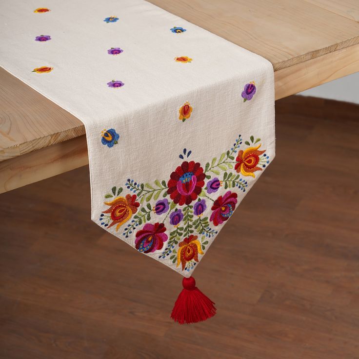 an embroidered table runner with flowers and tassels hanging from the edge on a wooden table