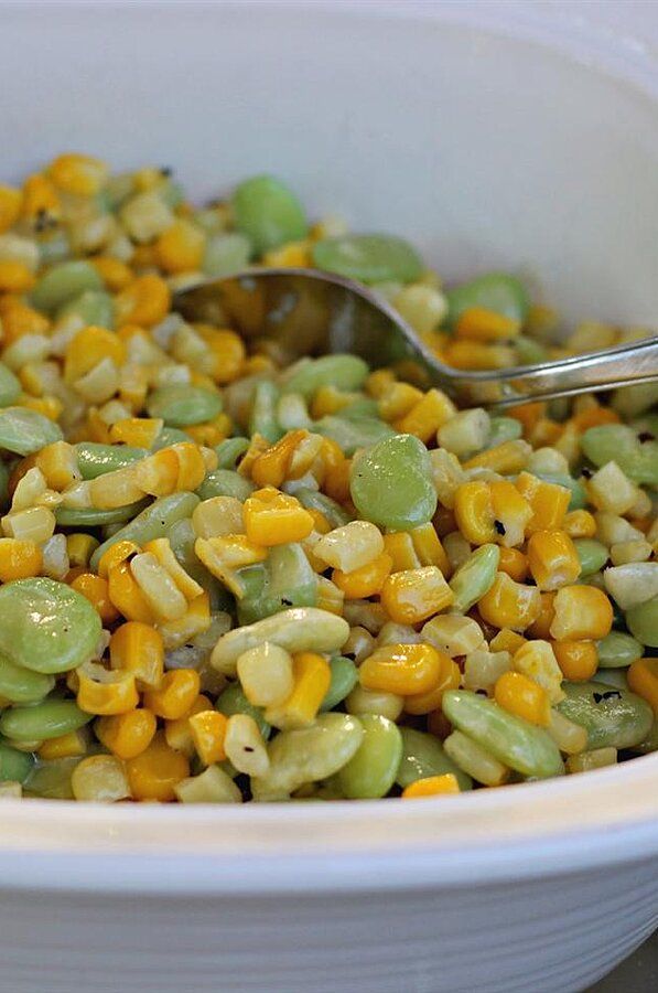 a white bowl filled with corn and green beans next to a metal spoon in it