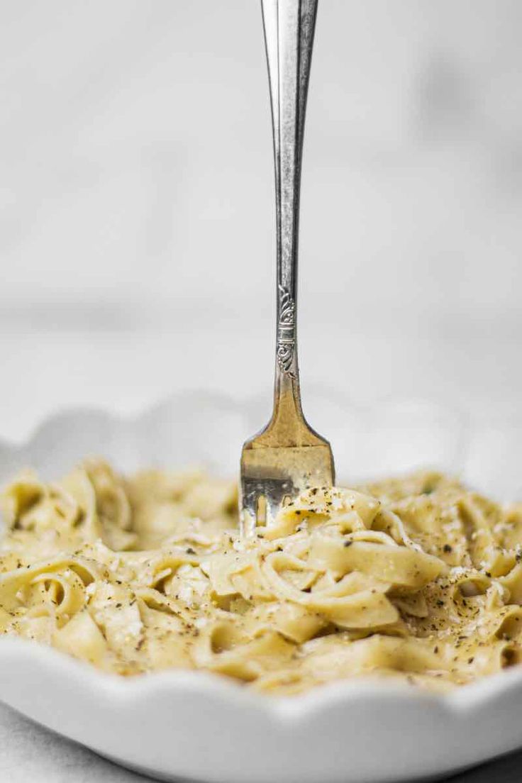 a fork is being used to stir pasta in a white bowl