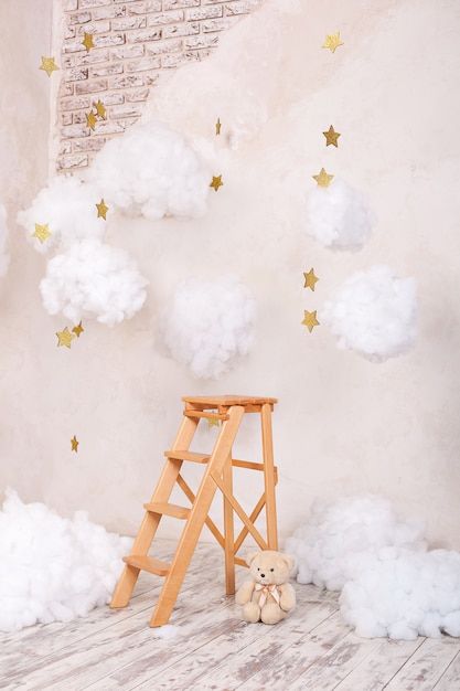 a teddy bear sitting next to a ladder in front of a wall with clouds and stars