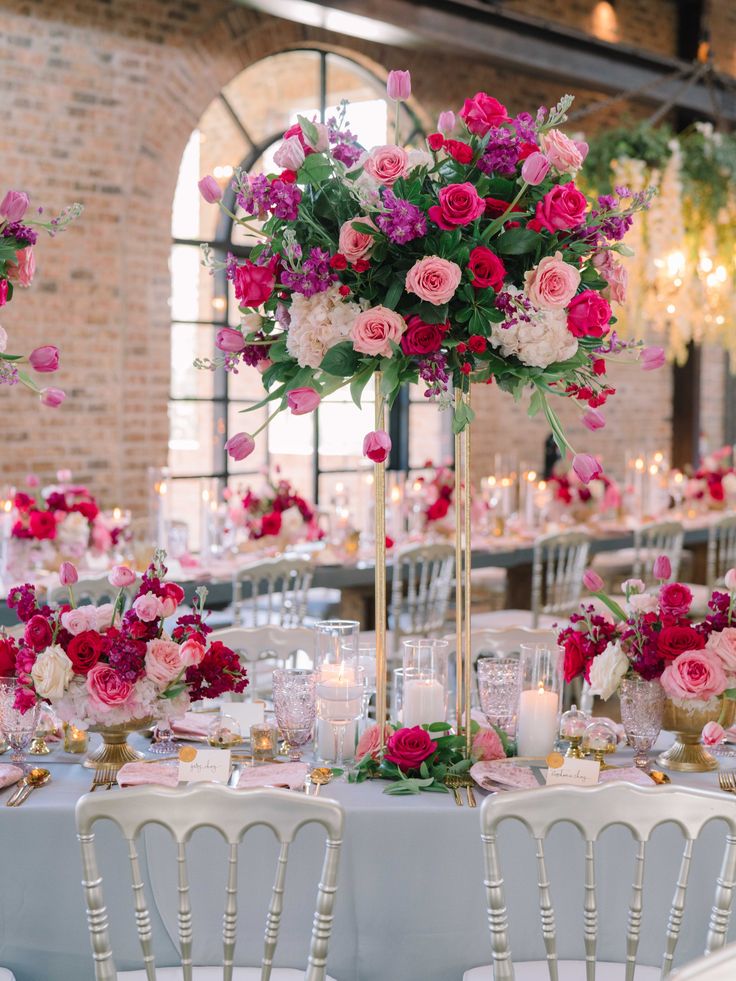 an elegant table setting with pink and red flowers in tall vases on the centerpiece