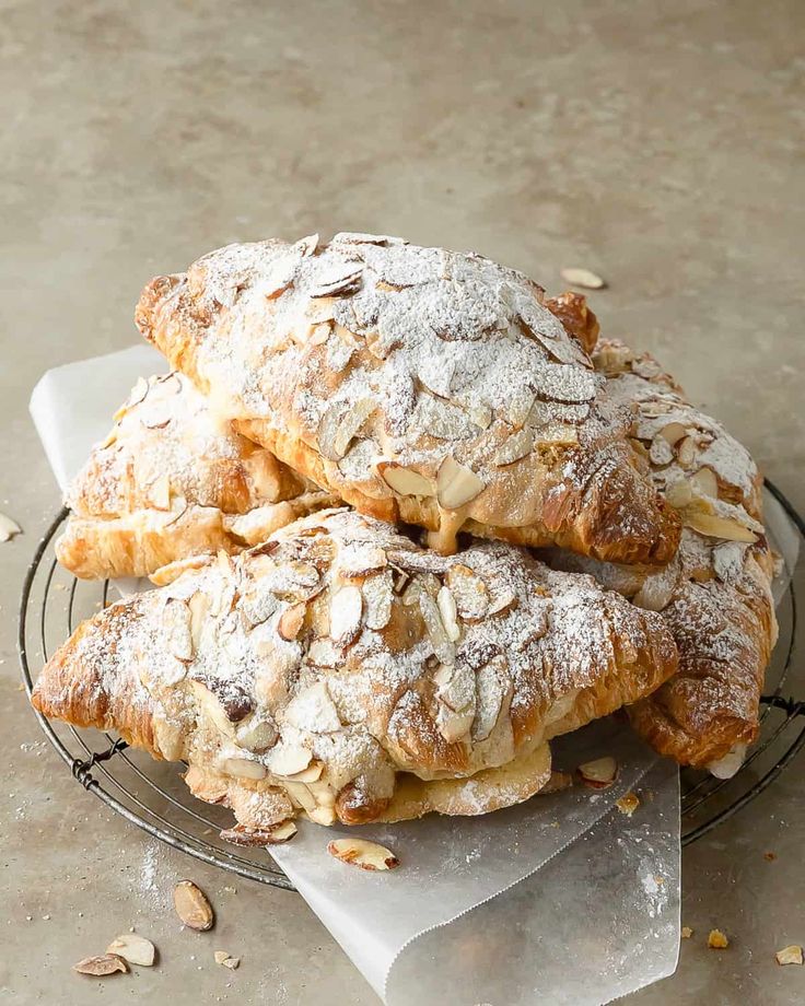 three pastries are piled on top of each other in a wire rack with powdered sugar and almonds