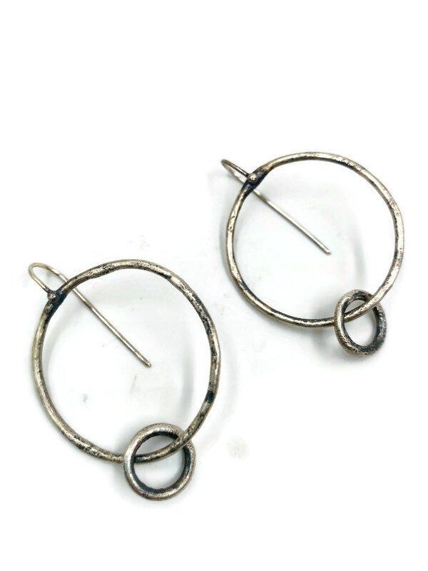 "These \"go to \" every day earrings are simple and beautiful . A circle that connects to a smaller ring that has a nice kinetic quality to them. They are organic in shape, slightly irregular ; crafted from textured sterling silver . Oxidised and brushed to a darker & satin finish. They measure 1 3/4\" long X 1 1/4\" wide." Contemporary Round Earrings, Contemporary Round Earrings For Everyday, Contemporary Everyday Round Earrings, Hand Forged Round Minimalist Earrings, Nickel-free Round Earrings With A Modern Twist, Modern Twist Round Earrings For Everyday, Minimalist Round Earrings With Oxidized Finish, Minimalist Oxidized Round Earrings, Contemporary Small Hoop Sterling Silver Earrings