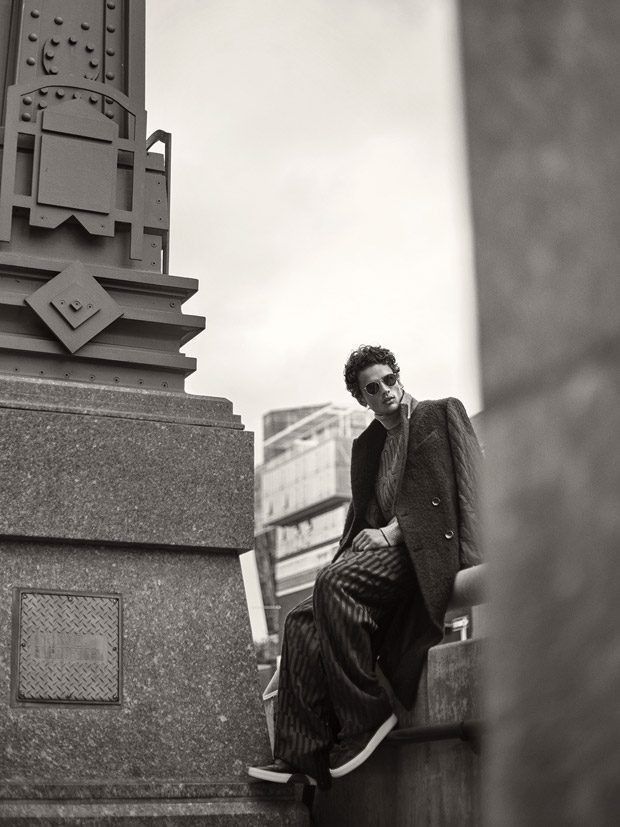 a man sitting on top of a stone pillar next to a tall clock tower in the city