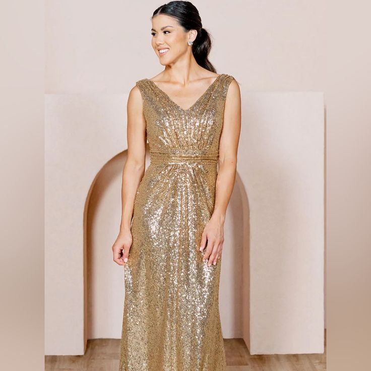 a woman in a gold sequin dress standing on a wooden floor smiling at the camera