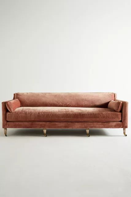 an orange velvet couch with gold legs and back rests against a white wall in front of it