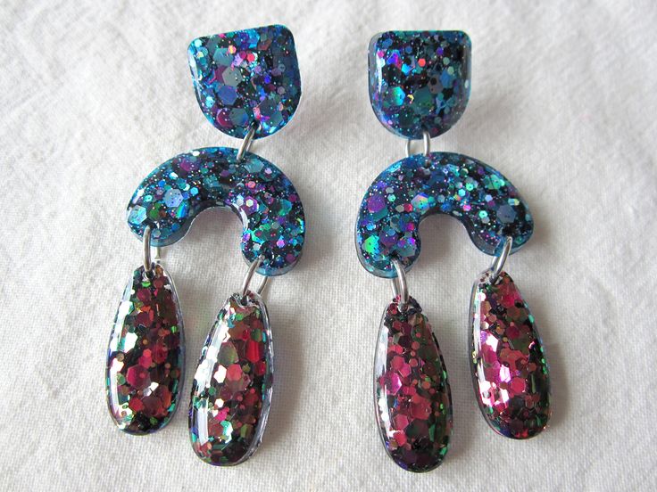 Sparkly and glittery resin earrings, arch shaped with rain drop shaped dangles at the bottom of the earring. The top part of the earring is a rounded square shape. These gorgeous statement earrings have a blue, purple holographic glitter and the rain drop shaped part is a watermelon holographic glitter with pink and green. This glitter really reflects and sparkles in the light. Great to wear for a night out , would make a fabulous gift. These earrings are light in weight and comfortable to wear Multicolor Glitter Dangle Earrings, Multicolor Glitter Drop Earrings, Blue Glitter Dangle Earrings, Blue Glitter Jewelry For Party, Pink Statement Earrings, Purple Holographic, Holographic Blue, Rounded Square, Holographic Glitter