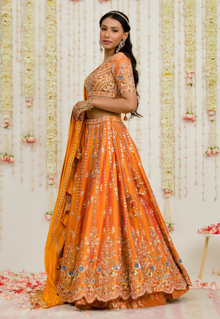 Editor's Note Rust Orange Mirror Thread And Zardosi Embroidered Raw Silk Lehenga. It Is Paired With A Matching Deep Neck Geometric Embroidered Blouse And Pure Silk Dupatta Fabric: Raw Silk, Silk Color: Rust Care: Dry Clean Only About the Designer Sanya Gulati's designs are inspired by the Indian bridesmaids, pastel easy hues & seasonal trends, her designs are a mix of modern, contemporary embroideries with traditional silhouettes thus creating our signature asymmetric checks embroideries amalgam Traditional Orange Embroidered Choli, Traditional Embroidered Orange Choli, Chanderi Embroidered Sets For Reception, Orange Anarkali Sets With Intricate Embroidery, Orange Saree Set With Intricate Embroidery, Orange Embroidered Sharara For Navratri, Designer Embroidered Orange Blouse Piece, Orange Choli With Intricate Embroidery For Festivals, Embroidered Orange Sharara For Navratri