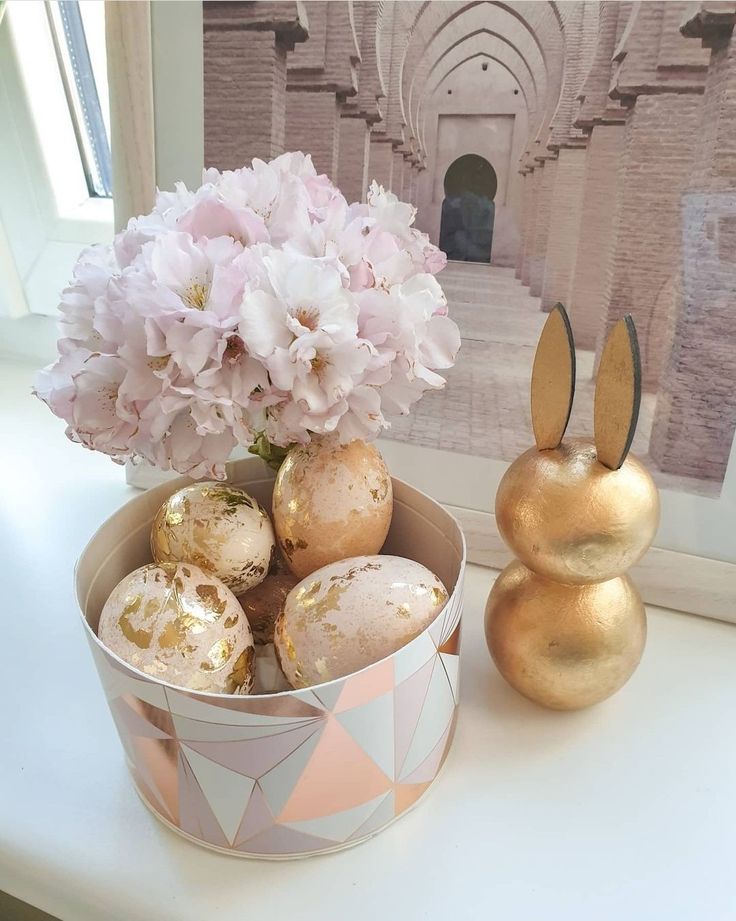 an easter basket with eggs and flowers on a table next to a gold bunny statue