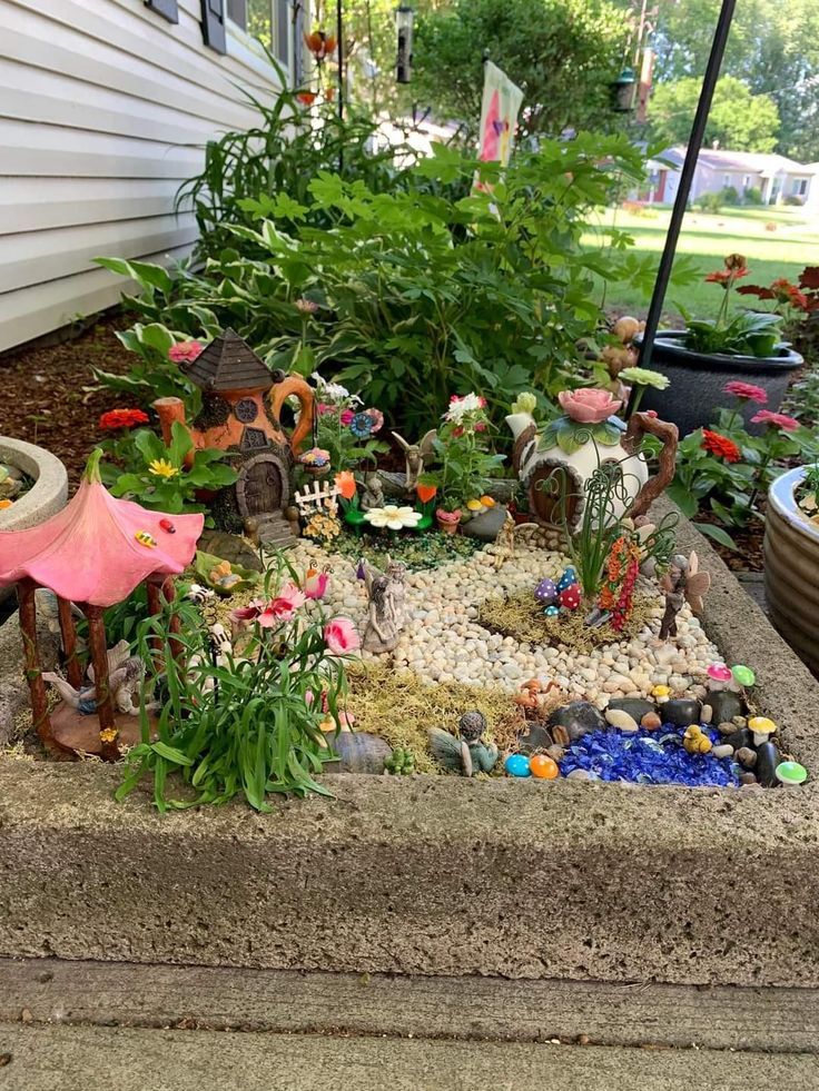 a small garden with lots of plants and rocks on the ground in front of a house