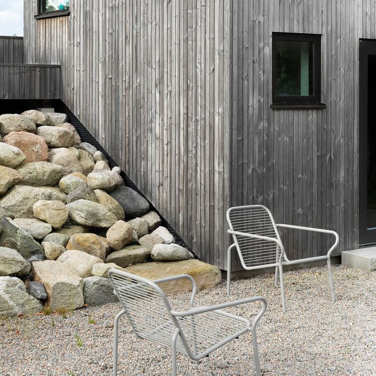 two chairs sitting next to each other in front of a building with rocks on the ground