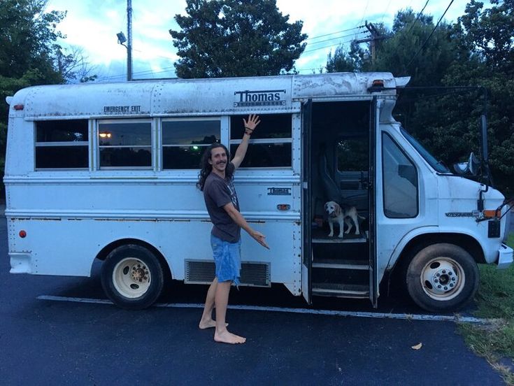 a man standing in front of a white bus with his hand up to the side