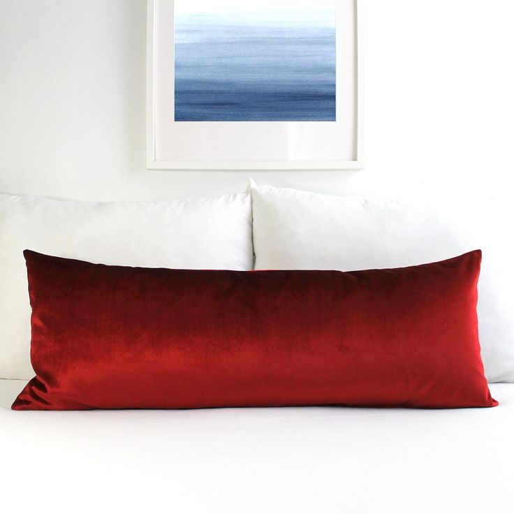 a red pillow sitting on top of a white bed next to a framed painting above it