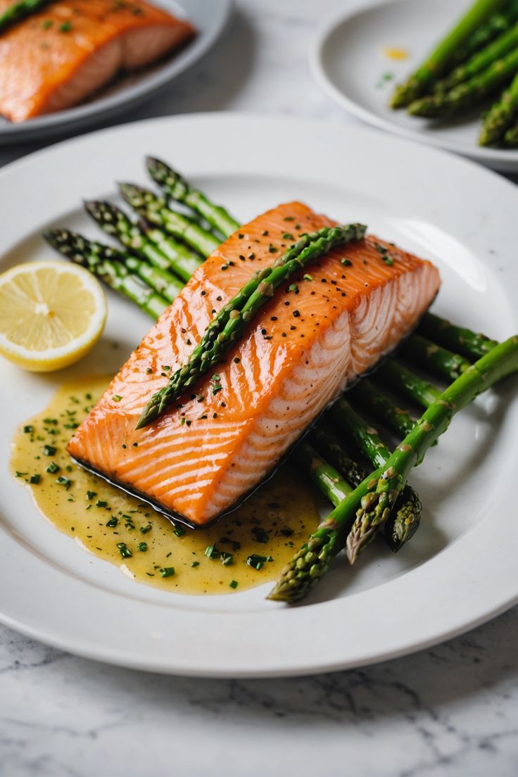 salmon and asparagus on a white plate with lemon wedges next to it