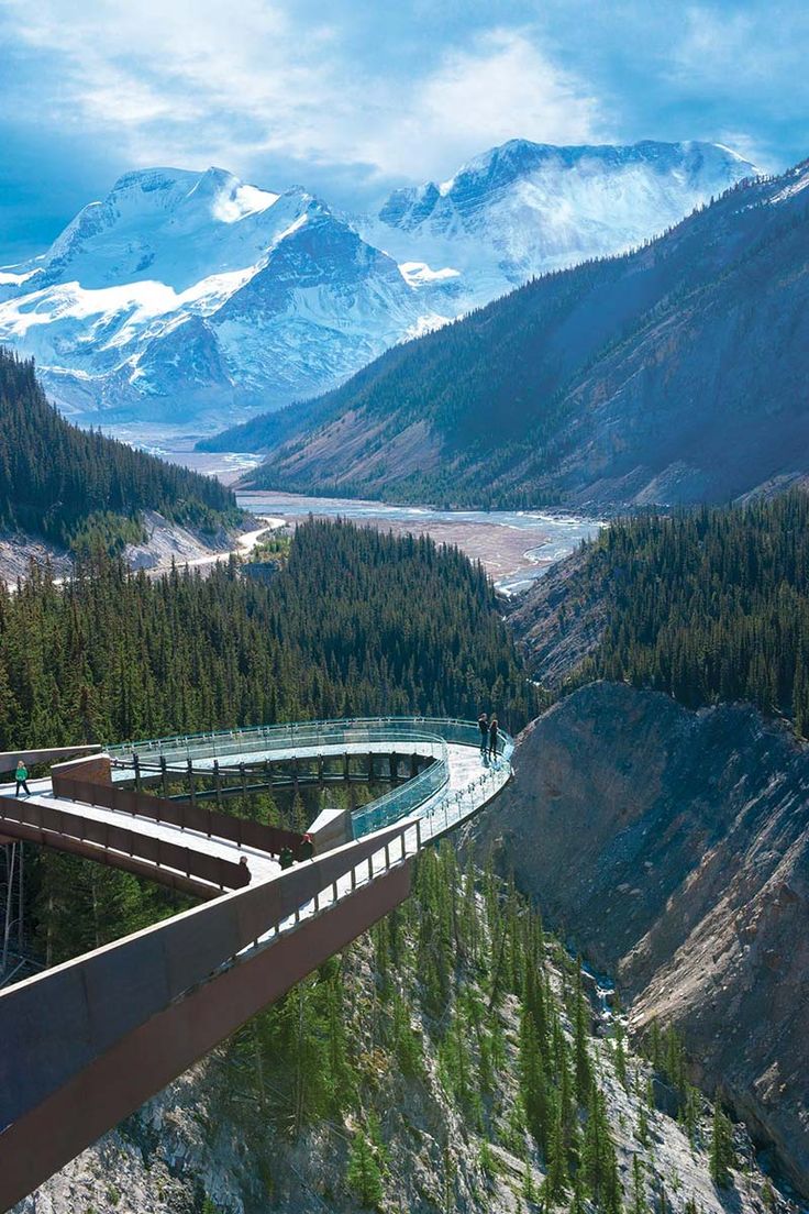 a bridge over a river with mountains in the background and people walking on one side