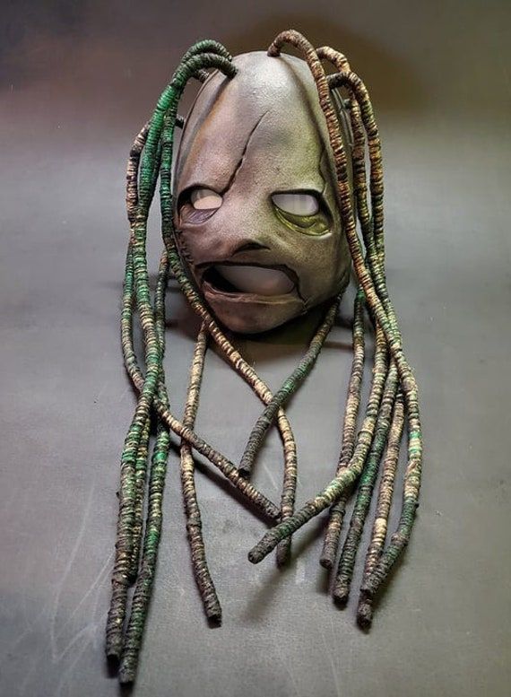 a weird looking mask with long hair and green beads on it's face, sitting on a table