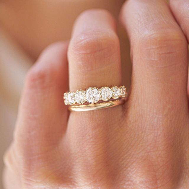 a woman's hand holding a gold ring with three diamonds on it and the band is