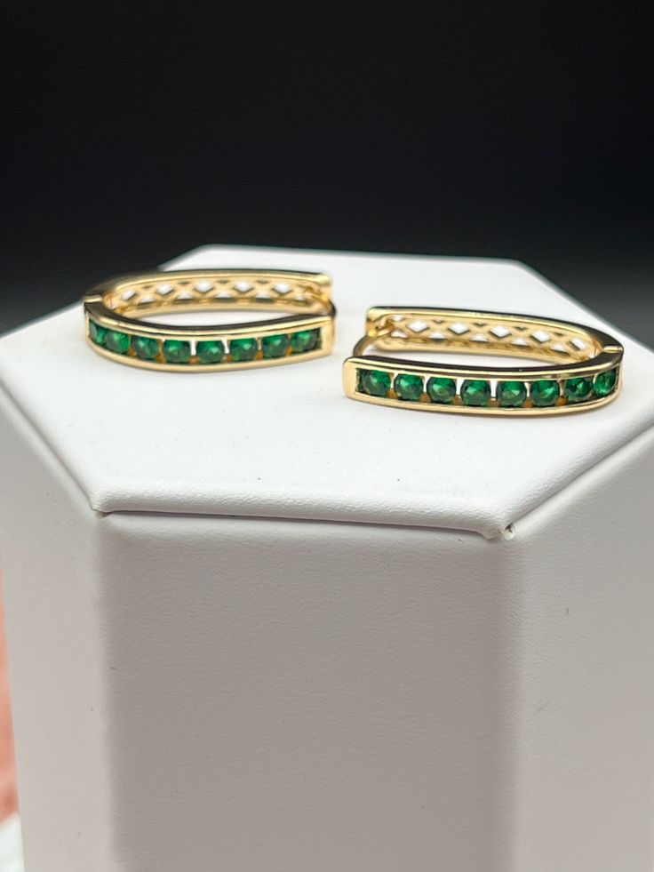 Emerald gold hoop earrings feature a circular design crafted in gold, adorned with multiple small, vivid green emeralds set along the outer edge. The emeralds sparkle elegantly, contrasting beautifully with the warm hue of the gold, creating a luxurious and sophisticated piece of jewelry. Green Round Gold-plated Earrings, Green Gold Plated Round Earrings, Green Gold-plated Round Earrings, Elegant Green Huggie Jewelry, Green Huggie Earrings With Matching Set, Green Formal Hoop Earrings, Formal Green Hoop Earrings, Elegant Gold Plated Green Hoop Earrings, Green Gold Plated Earrings For Anniversary