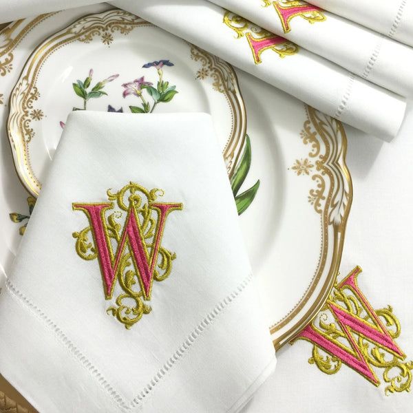 white napkins with gold trim and pink monogrammed letters on them, sitting next to each other